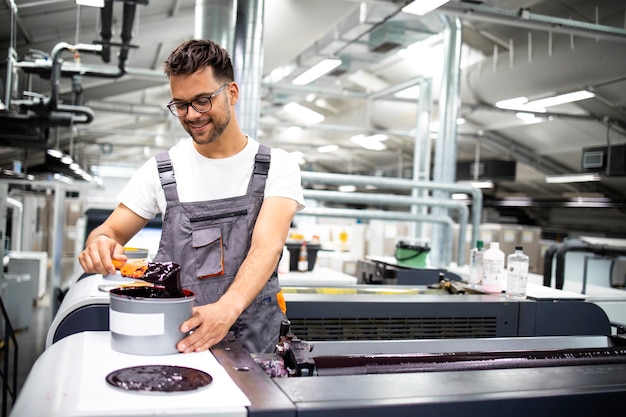 Operatore di macchina da stampa professionale che aggiunge più colore durante il processo di stampa in fabbrica.