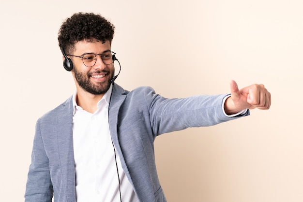 Operatore di telemarketer marocchino uomo che lavora con un auricolare isolato sul muro beige dando un pollice in alto gesto