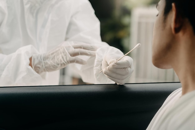 Operatore medico in tuta protettiva donna di screening Autista per campionare la secrezione per verificare la presenza di Covid19 controllo campione di tampone nasale campione dal paziente attraverso il finestrino dell'auto Diagnostica PCR xA