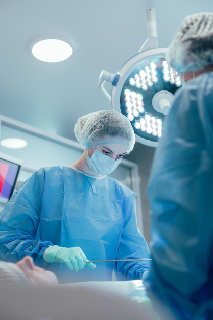 Operatore medico professionista che esegue un'operazione chirurgica insieme ai suoi colleghi e usa una pinza