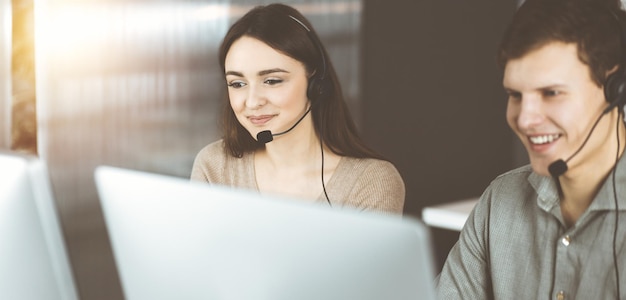 Operatori di call center al lavoro. Due giovani in cuffia stanno parlando con i clienti, seduti in un ufficio soleggiato