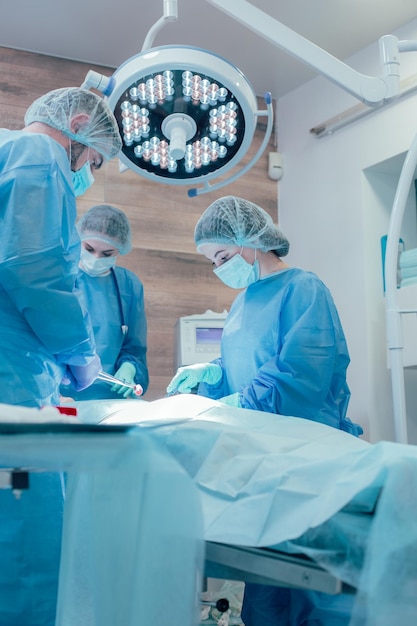 Operatori medici professionisti esperti in uniforme sterile che lavorano insieme con attenzione durante l'esecuzione dell'operazione chirurgica