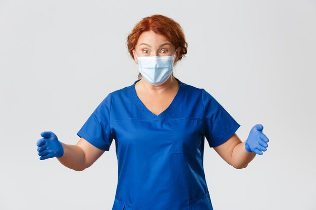 Operatori sanitari, pandemia, concetto di coronavirus. Dottoressa sorridente felice e stupita, infermiera in scrub e maschera per il viso, allarga le mani come se tenesse qualcosa di grande, mostra grandi dimensioni.