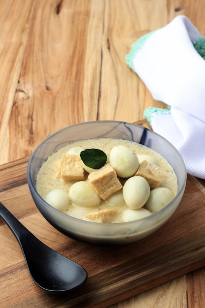 Opor Tahu Telur Puyuh o curry indonesiano con tofu e uovo di quaglia servito su una ciotola di ceramica su un tavolo di legno