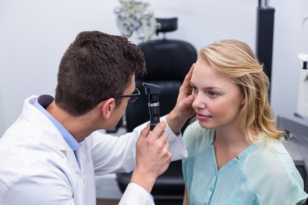 Optometrista che esamina paziente femminile attraverso l'oftalmoscopio