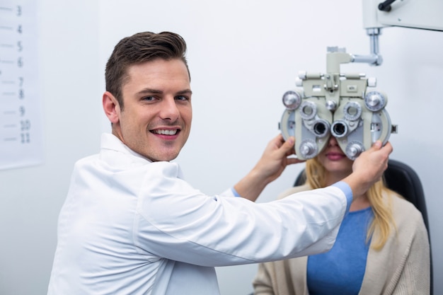 Optometrista sorridente che esamina paziente femminile su phoropter