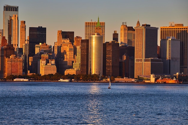 Ora d'oro sullo skyline di Manhattan New York City dalle acque con singola nave e riflesso della luce del sole