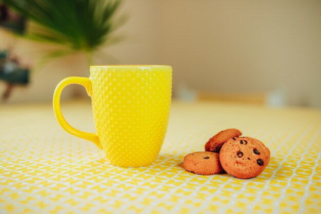 Ora del tè, tazza di tè gialla e biscotti sul tavolo.