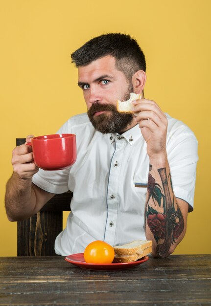 Ora di colazione. Colazione pranzo cena. L'uomo barbuto mangia dal piatto rosso. Tempo del caffè. Mattina. Routine mattutina.