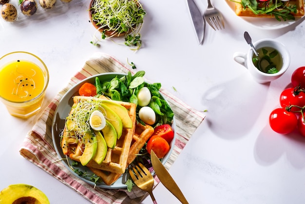 Ora di colazione. Waffle con insalata, uova, succo e avocado per colazione.