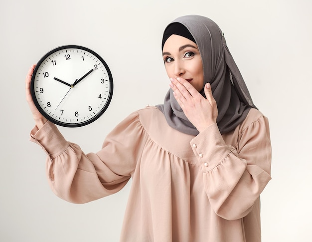 È ora di fare in fretta. Donna saudita che tiene l'orologio a baclground bianco