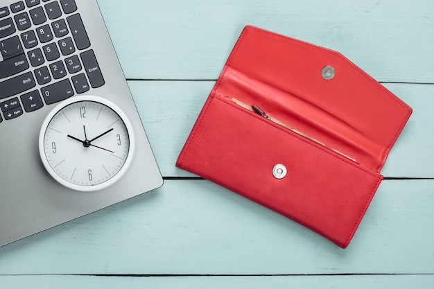 È ora di fare soldi Affari online. Orologio bianco, laptop e portafoglio rosso su superficie di legno blu. Colpo minimalista dello studio. Vista dall'alto