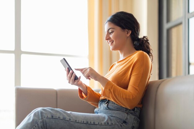 Ordina online una giovane donna indiana felice che usa lo smartphone a casa