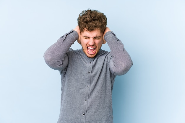 Orecchie di copertura isolate giovane uomo caucasico dei capelli ricci biondi con le mani che provano a non sentire il suono troppo forte.