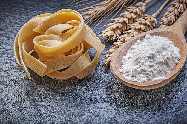 Orecchie di segale di grano cucchiaio di legno farina di pasta cruda su sfondo nero concetto di cibo e bevande