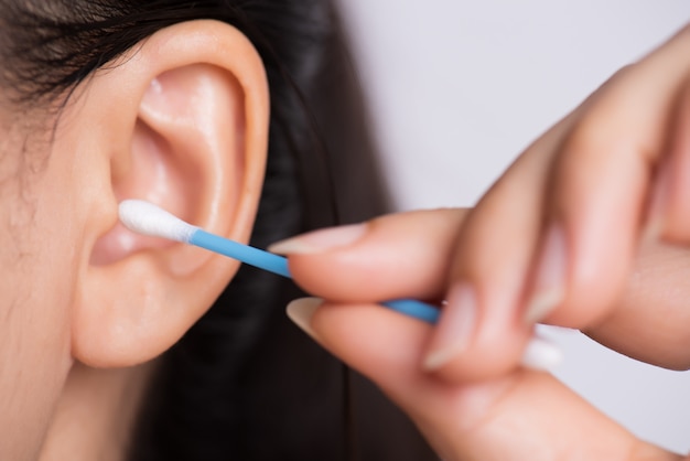 Orecchio di pulizia donna con un batuffolo di cotone. Sanità e concetto di pulizia dell&#39;orecchio.