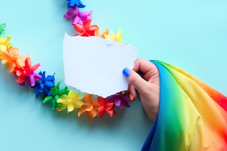 Foto orgoglio della comunità lgbtq testo io sono gay su carta in mano con bandiera arcobaleno ghirlanda di fiori e unghie finte nei colori dell'arcobaleno concept shot vista piatta dall'alto su sfondo blu menta