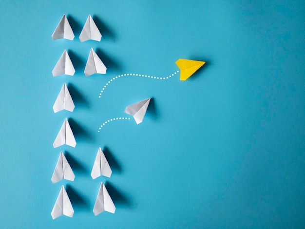 Origami di aeroplani di carta gialla e bianca che lasciano altri aeroplani bianchi su sfondo blu con spazio personalizzabile per il testo Concetto di capacità di leadership