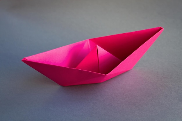Origami di barchetta di carta rosa isolato su sfondo grigio