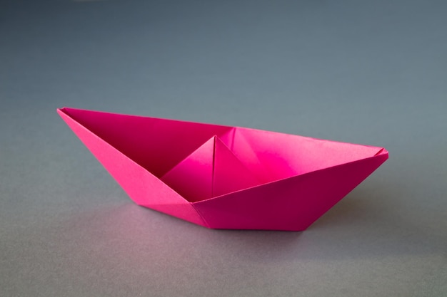 Origami di barchetta di carta rosa isolato su sfondo grigio