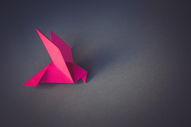 Origami di colomba di carta rosa isolato su sfondo grigio