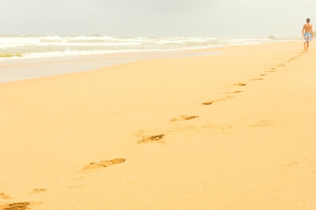 Orme sulla spiaggia deserta con un uomo sullo sfondo in una mattina nuvolosa a Bentota Sri Lanka