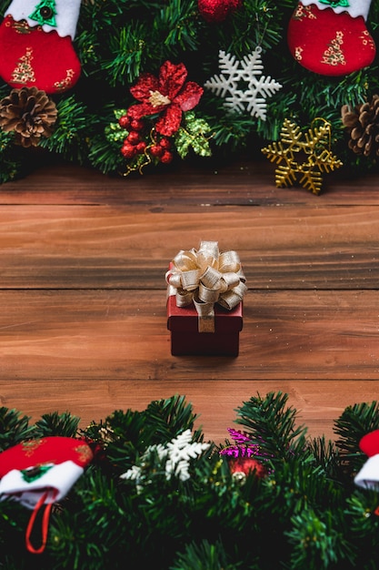 Ornamenti di Natale docorate al confine di fondo in legno naturale. Una bellissima scatola regalo lucida con un nastro dorato incastonato nel mezzo. Spazio vuoto per la formulazione.