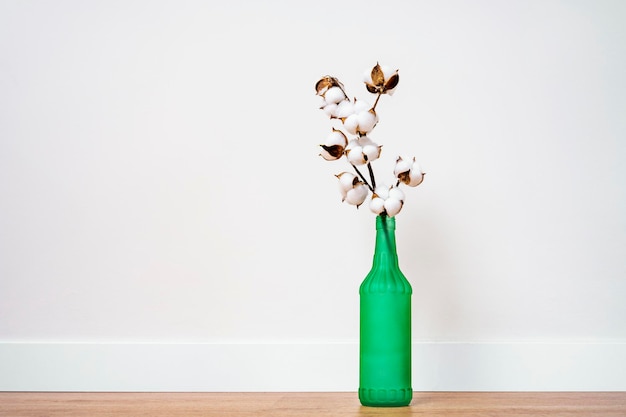 Ornamento floreale per l'interior design con bottiglia verde e ramo di cotone su fondo marrone