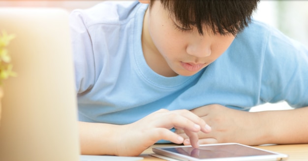 Orologio asiatico sveglio del ragazzo e giocare su tablet PC.