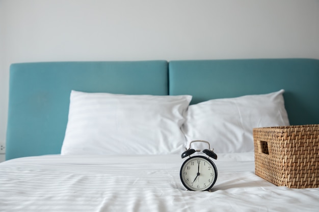 Orologio classico sul letto bianco con il canestro di legno sul letto in camera da letto.