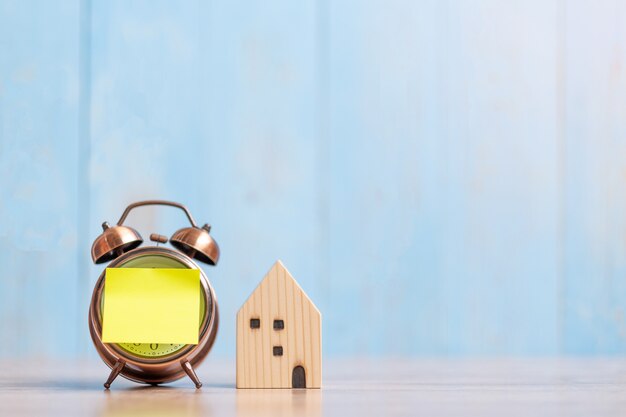 Orologio con nota di carta e modello di casa su legno