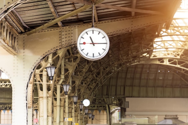 Orologio d'epoca sulla stazione ferroviaria con il tetto dell'edificio.