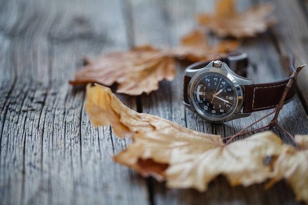 Orologio da polso su tavola di legno con foglia d'autunno