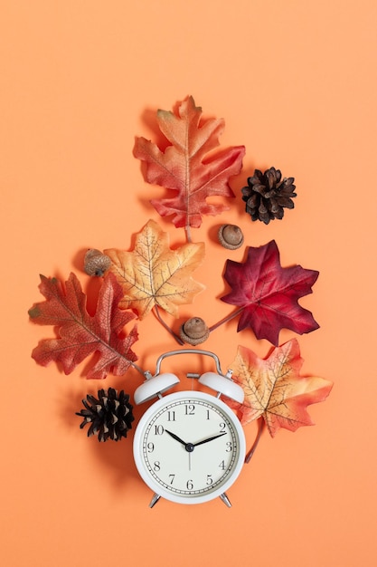 Orologio e foglie vista dall'alto su sfondo arancione. Tempo d'autunno