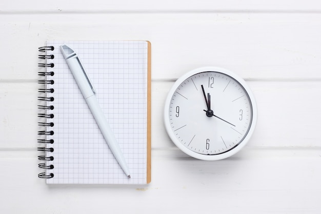 Orologio e taccuino bianchi su superficie di legno bianca. Colpo minimalista dello studio. Vista dall'alto