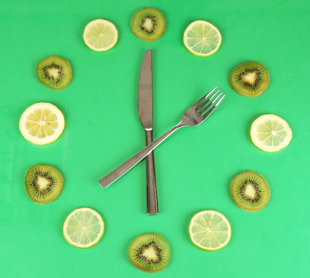 Orologio fatto di kiwi lime e fette di limone su sfondo colorato