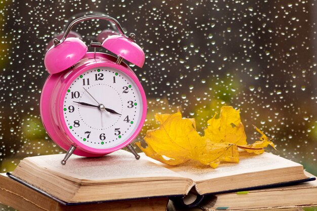 Orologio, foglie secche autunnali e libri sullo sfondo di un vetro bagnato