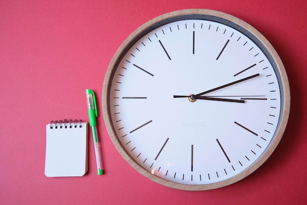 Orologio isolato su sfondo magenta con taccuino e penna visto da vicino