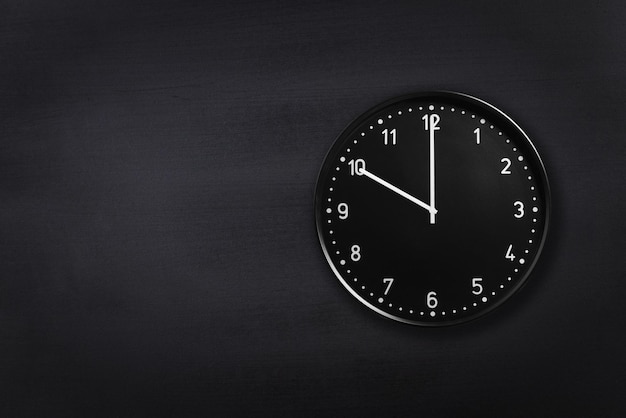Orologio nero che mostra le dieci su sfondo nero della lavagna Orologio da ufficio che mostra le 10:00 o le 22:00