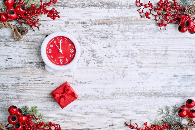 Orologio sullo sfondo su un tavolo di legno decorato con una ghirlanda e palline di Natale rosse per il nuovo anno o Natale. Copia spazio