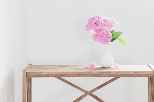 Ortensia rosa in vaso bianco sullo scaffale di legno sulla parete bianca del fondo