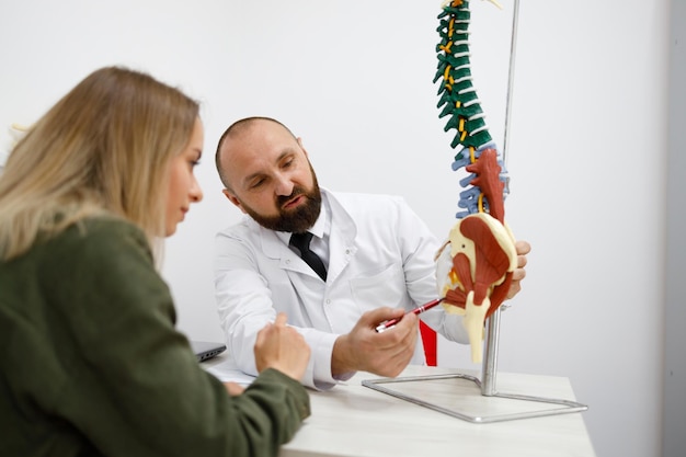 Ortopedico che mostra il modello della colonna vertebrale a una paziente in ospedale