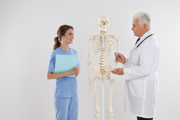 Ortopedico professionista con modello di scheletro umano che insegna studente di medicina su sfondo chiaro