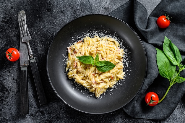 Orzo con salsa di panna, pancetta e basilico. Risoni preparati. Sfondo nero. Vista dall'alto