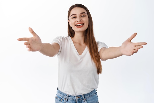 Ospite femminile sorridente e amichevole, allunga le mani e invita, raggiunge l'abbraccio, accoglie gli ospiti, vuole abbracciarti e abbracciarti, accogliere gli amici, in piedi su sfondo bianco