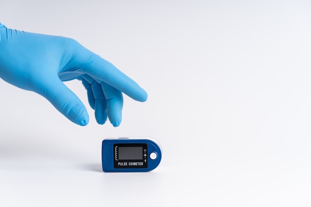 Ossimetro da polso su sfondo bianco. Una mano in un guanto medico tiene un dispositivo per la diagnostica sanitaria.