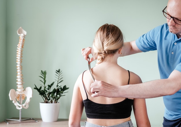 Osteopata che esegue manipolazioni di rilascio della fascia utilizzando il trattamento IASTM, ragazza che riceve un trattamento dei tessuti molli sul collo con uno strumento in acciaio inossidabile