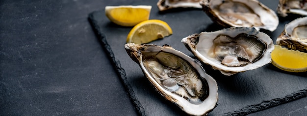 Ostriche fresche con limone servite su piatto nero. Dieta di pesce di lusso