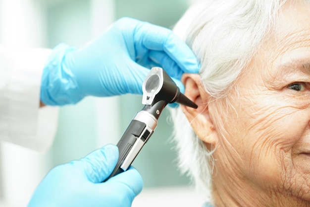 Otorinolaringoiatra o medico ORL che esamina l'orecchio di un paziente anziano con problema di perdita dell'udito all'otoscopio