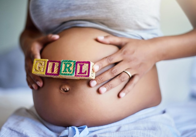 Ottenere il regalo di una bambina Ripresa ritagliata di una donna incinta con blocchi di legno sul ventre che compongono la parola ragazza